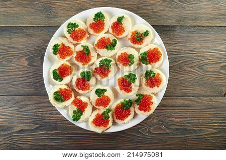 Top view horizontal shot of a plate with buttered canapes with red caviar decorated with greens copyspace luxury expensive dish food eating healthy delicious appetizer restaurant.