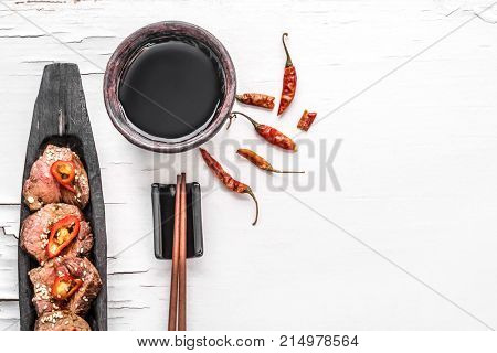 Slices of oriental spicy meat with sesame seads and pepper on long dark wooden plate with chopsticks the white wooden surface with cracked paint. Top view. Place for text.