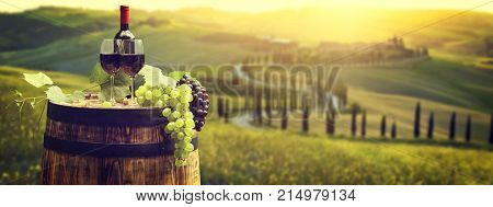 Red wine bottle and wine glass on wodden barrel. Beautiful Tuscany background