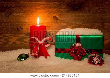 A gift wrapped Christmas present with candle and snow against a wooden background.