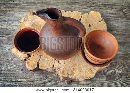 A Traditional Georgian Wine Jug And Clay Cups Filled With A Red Wine On The Wooden Table With Grapes
