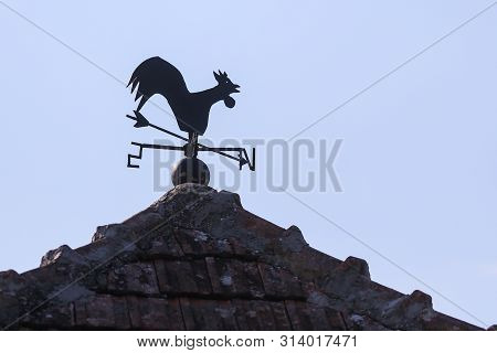 A Weather Vane (or Wind Vane, Weathercock) On Top Of A Building In A Rural Area