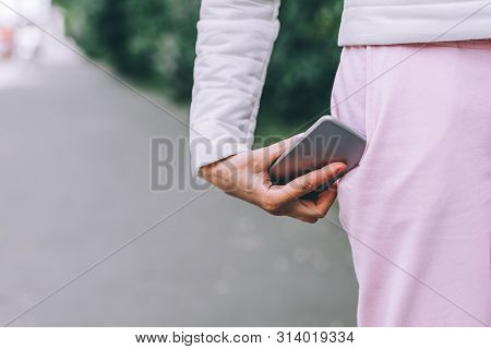 Close Up Of Womans Hand In White Jacket Catches Smartphone Falling Out Of Pink Sports Pants Pocket. 