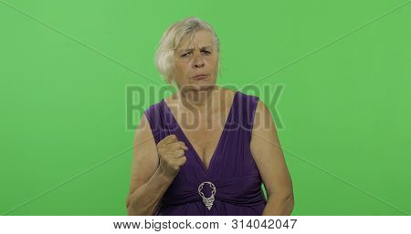 An Elderly Woman Quarrels At Someone. Old Unkind Grandmother Scolding In A Purple Dress. Place For Y