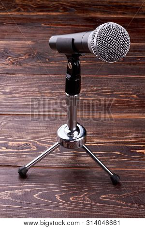 Microphone On Brown Wooden Background. Microphone On Short Rack Stand, Vertical Image.