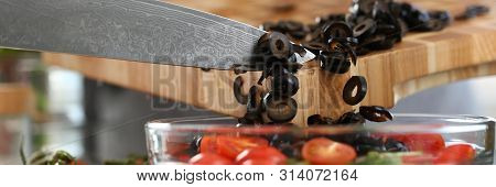 Chef Pouring Round Pieces Black Olive Salad Bowl. Man Chopping Vegetable On Wooden Cutting Board At 