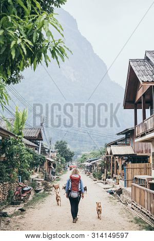 Young Caucasian Blonde Woman With Backpack Walking On The Central Street Of Muang Ngoi Village, Laos