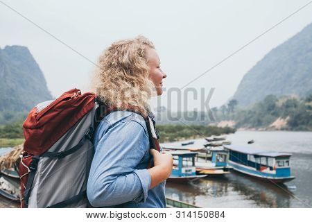 Caucasian Blonde Woman With Backpack Stands On Boat Pier In Muang Ngoi Village, Laos