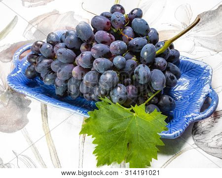 Bunch Of Ripe Blue-black Table Grapes With Leaf Served On Blue Plate As Sweet Fruit Dessert