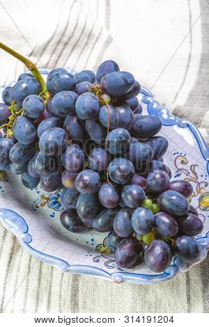 Bunch Of Ripe Blue-black Table Grapes With Leaf Served On Blue Plate As Sweet Fruit Dessert