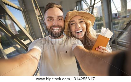 Travelling Concept. Couple Making Selfie At Airport Terminal, Woman Holding Passports With Tickets
