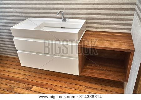 Wall mounted bathroom vanity in luxury bathroom with teak floor and striped tiles. Stylish interior of modern bathroom. Details furniture