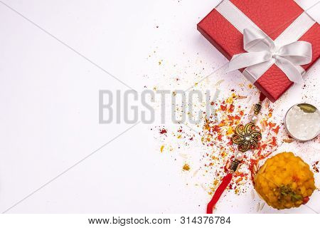 A Red Gift Box, Elegant Rakhi And Sweet With Spread Rice Grains, Kumkum And Haldi On White Backgroun