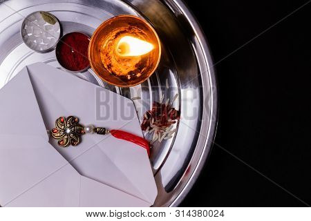 Indian Festival Concept- Rakhi In A White Envelope With Rice Grains, Kumkum And Diya On A Plate With