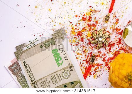 Indian Festival - Elegant Rakhi, Sweet And Indian Currency Notes With Scattered Rice Grains, Kumkum,