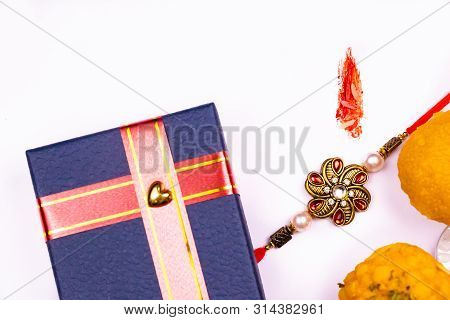 Raksha Bandhan -  Elegant Rakhi, Sweets And Blue Gift Box With Kumkum And Rice Grain Mark On A White