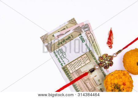 Raksha Bandhan Concept - A Traditional Indian Wrist Band, Sweets With Rice Grains And Kumkum Mark An