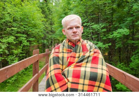 Caucasian Male Blond Stands On A Wooden Trail In A Checkered Plaid. Around Him Are Trees, Plants. Th