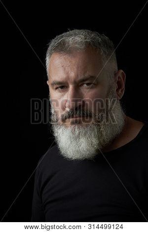 Portrait Of A Brutal Gray Haired Man With A Gray Lush Beard And Strict Face On A Black Background, S