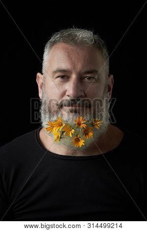 Portrait Of A Smiling Brutal Man With A Gray Beard Decorated With Yellow Flowers On A Black Backgrou