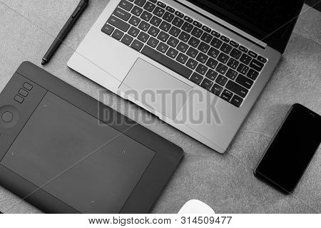 Workplace With Open Laptop With Black Screen, Mouse, Graphics Tablet And Smart Phone On Modern Grey 