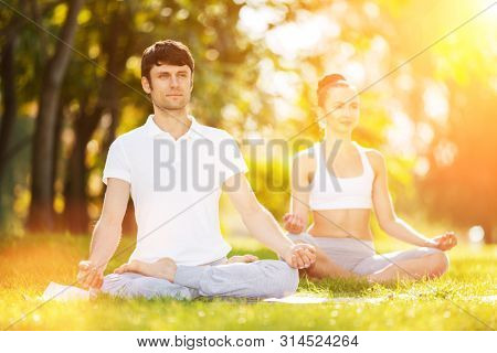 Couples Yoga, man and woman doing yoga exercises, meditate in sunny the park. Yoga outdoor. Concept of healthy lifestyle and relaxation. Yoga meditation in nature. Couple practicing on the grass
