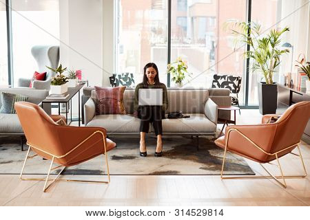 Businesswoman Sitting On Sofa Working On Laptop At Desk In Shared Workspace Office