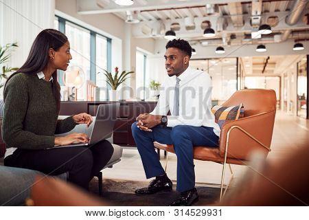 Businesswoman Interviewing Male Job Candidate In Seating Area Of Modern Office