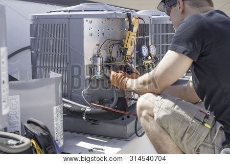 Hvac Repair Technician Using A Volt Meter To Test Components On An Air Conditioner Condenser.