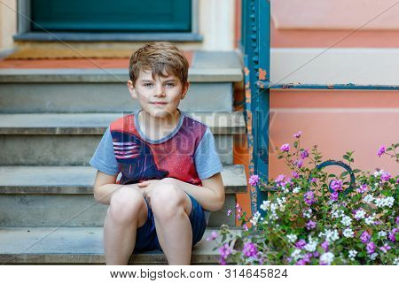 Portrait Of Lovely Gorgeos School Kid Boy Sitting Infront Of House. Happy Healthy Boy On Stairs By H