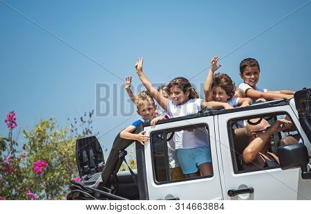 Happy children having fun in the car, cheerful kids standing in the open-top vahicle, enjoying summertime road trip