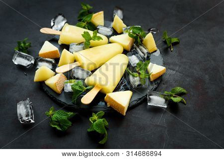 Homemade Melon Ice Cream, Pops Or Popsicles With Ice, Melon Slices And Mint On Round Dark Slate Plat