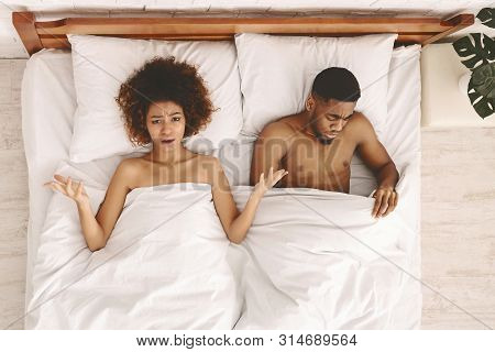 Sex Problem. Disappointed Black Unsatisfied Woman Lying In Bed, Sad Man Looking Under Blanket, Top V
