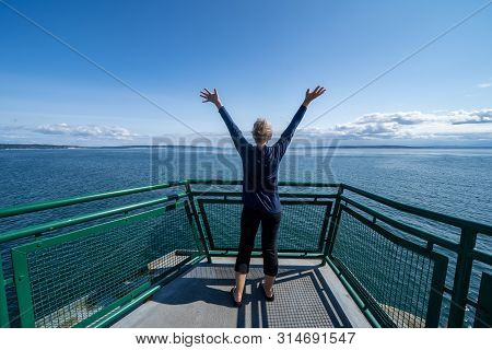Woman Passenger On The Port Townsend Ferry In Washington State Stands With Her Arms Up And Back To T