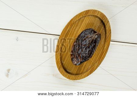 One Whole Dried Brown Date Medjool On Bamboo Plate Flatlay On White Wood