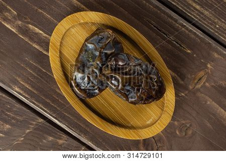 Group Of Two Whole Dried Brown Date Medjool On Bamboo Plate Flatlay On Brown Wood