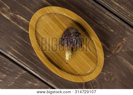 One Half Of Dried Brown Date Medjool On Bamboo Plate Flatlay On Brown Wood