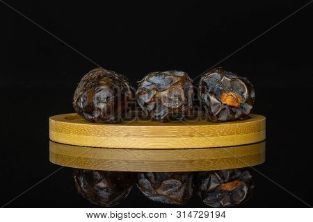 Group Of Three Whole Dried Brown Date Medjool On Bamboo Plate Isolated On Black Glass