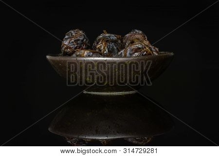 Lot Of Whole Dried Brown Date Medjool On Grey Ceramic Plate Isolated On Black Glass