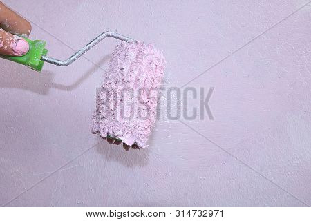 A Hand With A Roller On The Background Of A Painted Wall. Painting The Walls During The Repair And M