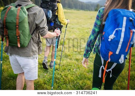 Gorup Of Friends Climbing Up Hill, With Backpacks And Climbing Stick