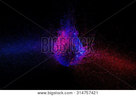 high speed photography. image of the explosion of a balloon filled with water and taken at the exact moment of the impact. blue and purple lights.