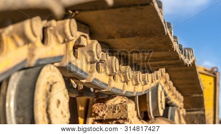 Panorama Frame Close Up Of The Dirty Track Pad And Rollers Of A Yellow Excavator On A Sunny Day
