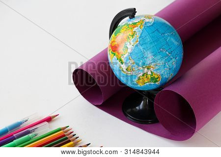 Globe On Purple Cardboard On A White Background With Colored Pencils. Back To School Concept