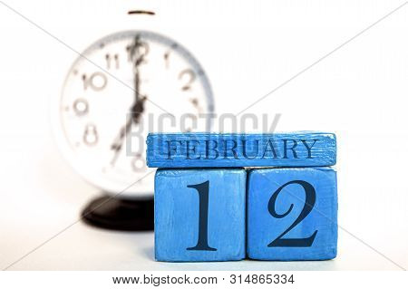 February 12th. Day 12 Of Month, Handmade Wood Calendar And Alarm Clock On Blue Color. Winter Month, 