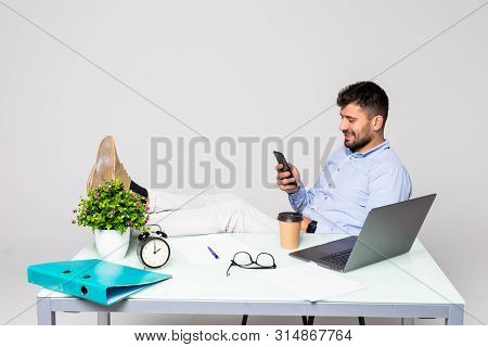 Cheerful Young Successful Man Is Talking On The Phone At The Workplace With Feet On The Table.he Is 