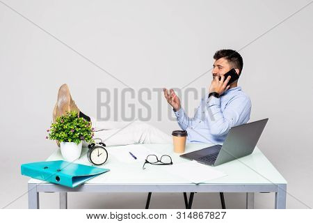 Cheerful Young Successful Man Is Talking On The Phone At The Workplace With Feet On The Table.