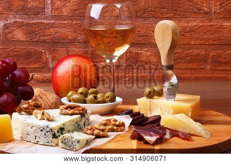 Assortment Of Cheese With Fruits, Grapes, Nuts And Cheese Knife On A Wooden Serving Tray.
