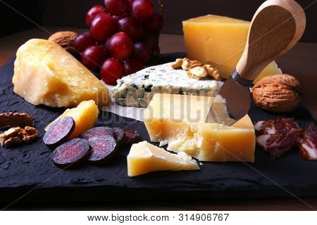 Assortment Of Cheese With Fruits, Grapes, Nuts And Cheese Knife On A Wooden Serving Tray.