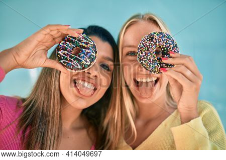 Two beautiful and young girl friends together having fun with tasty dougnut